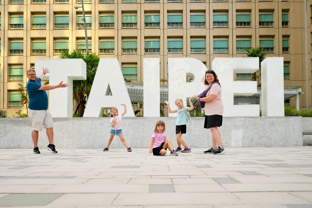 The whole Clarkson family posed in front of a large Taipei sign on a sunny day in Taipei, Taiwan
