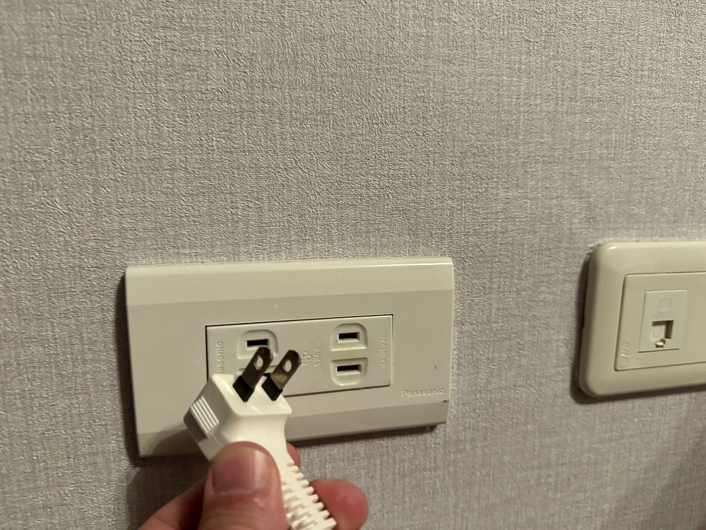 A US-style Type A two-pin power outlet on a wall in Taiwan with a laptop nearby, showing American plugs work without an adapter