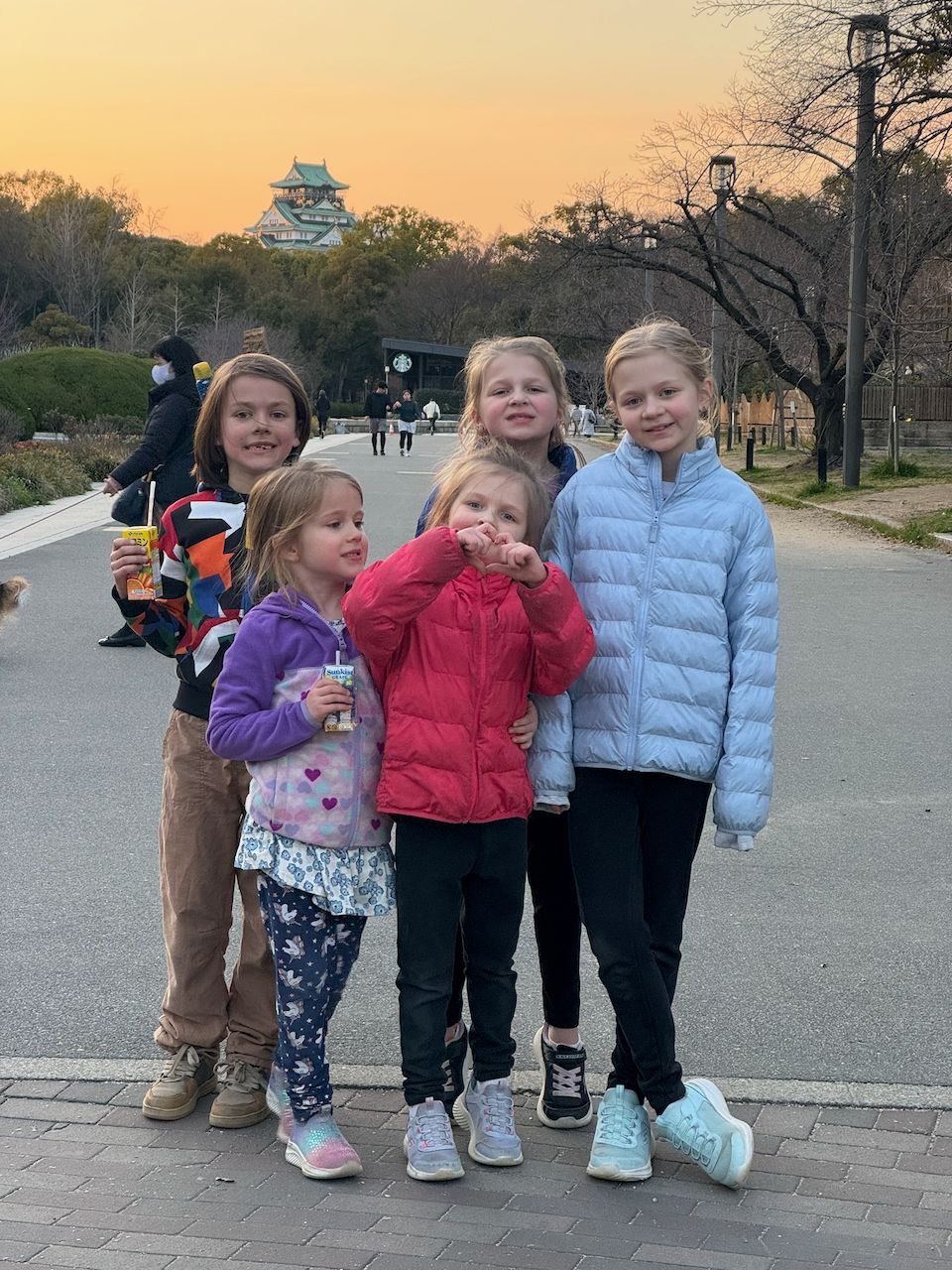 Cora, Harper, and Lily at Osaka Castle at golden hour with juice boxes