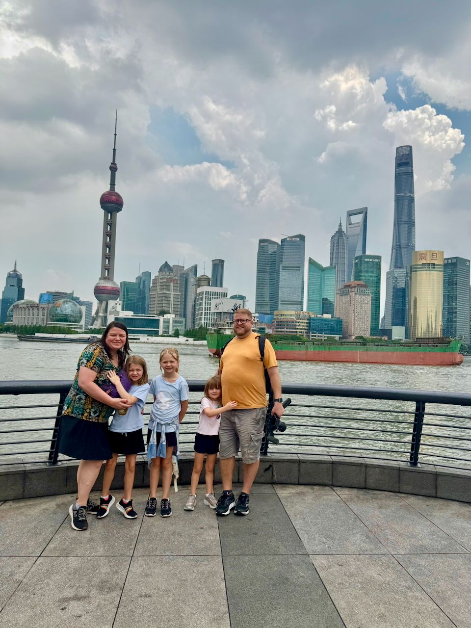 Adam, Lindsay, Lily, Cora, and Harper posing on the Bund promenade in Shanghai with the Pudong skyline and Oriental Pearl Tower behind them