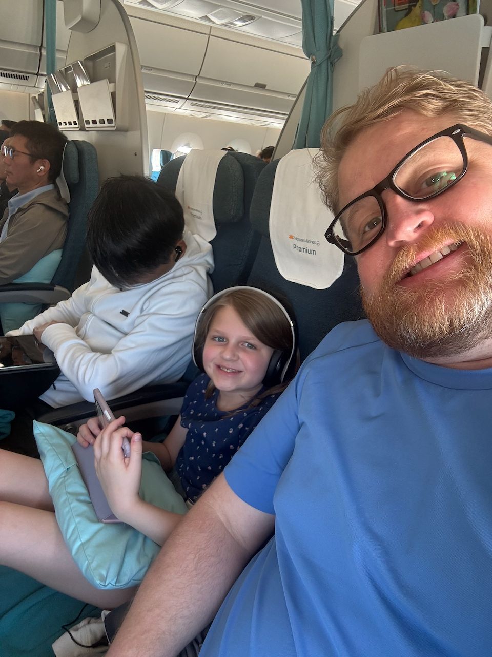 Adam takes a selfie on a Vietnam Airlines flight with two of his daughters watching iPads in the background