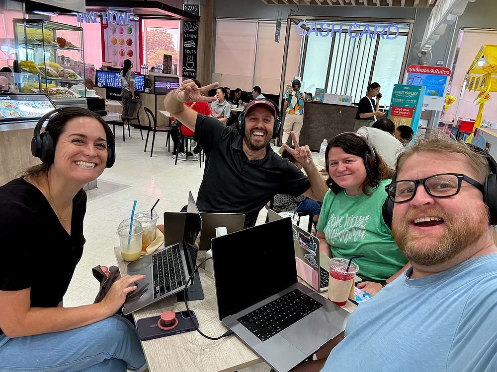 Four adults with laptops and iced drinks working at a table in a Chiang Mai mall food court