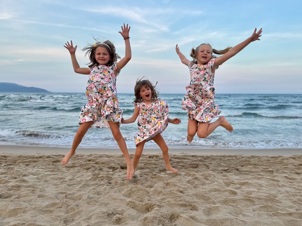Lily, Cora, and Harper jumping on the beach at My Khe in matching floral dresses