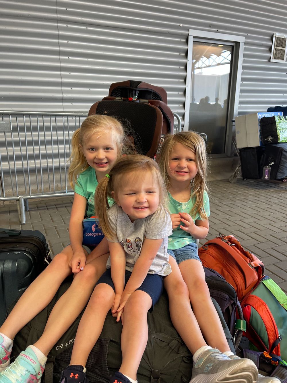 Cora, Harper, and Lily sitting on top of luggage piled outside the Southampton cruise terminal
