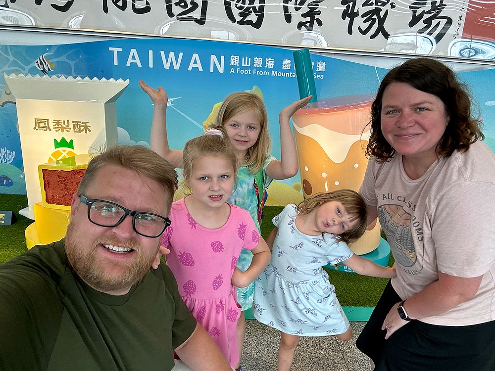 All five Clarksons taking a selfie in front of the giant pineapple cake and bubble tea welcome display at Taoyuan International Airport