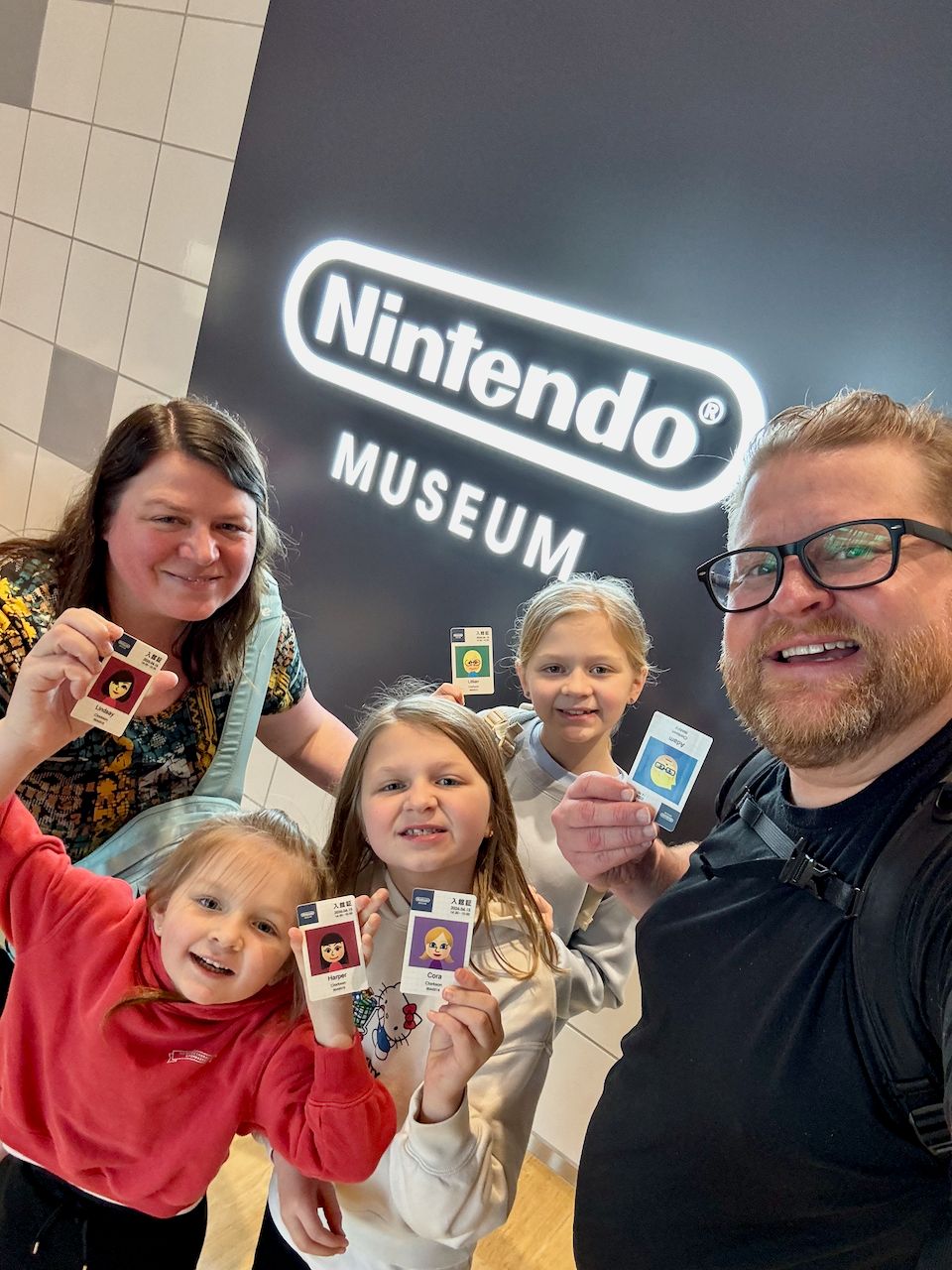 Adam, Lindsay, Lily, Cora, and Harper stand in front of the illuminated Nintendo Museum sign in Uji, Japan, each holding a commemorative ticket
