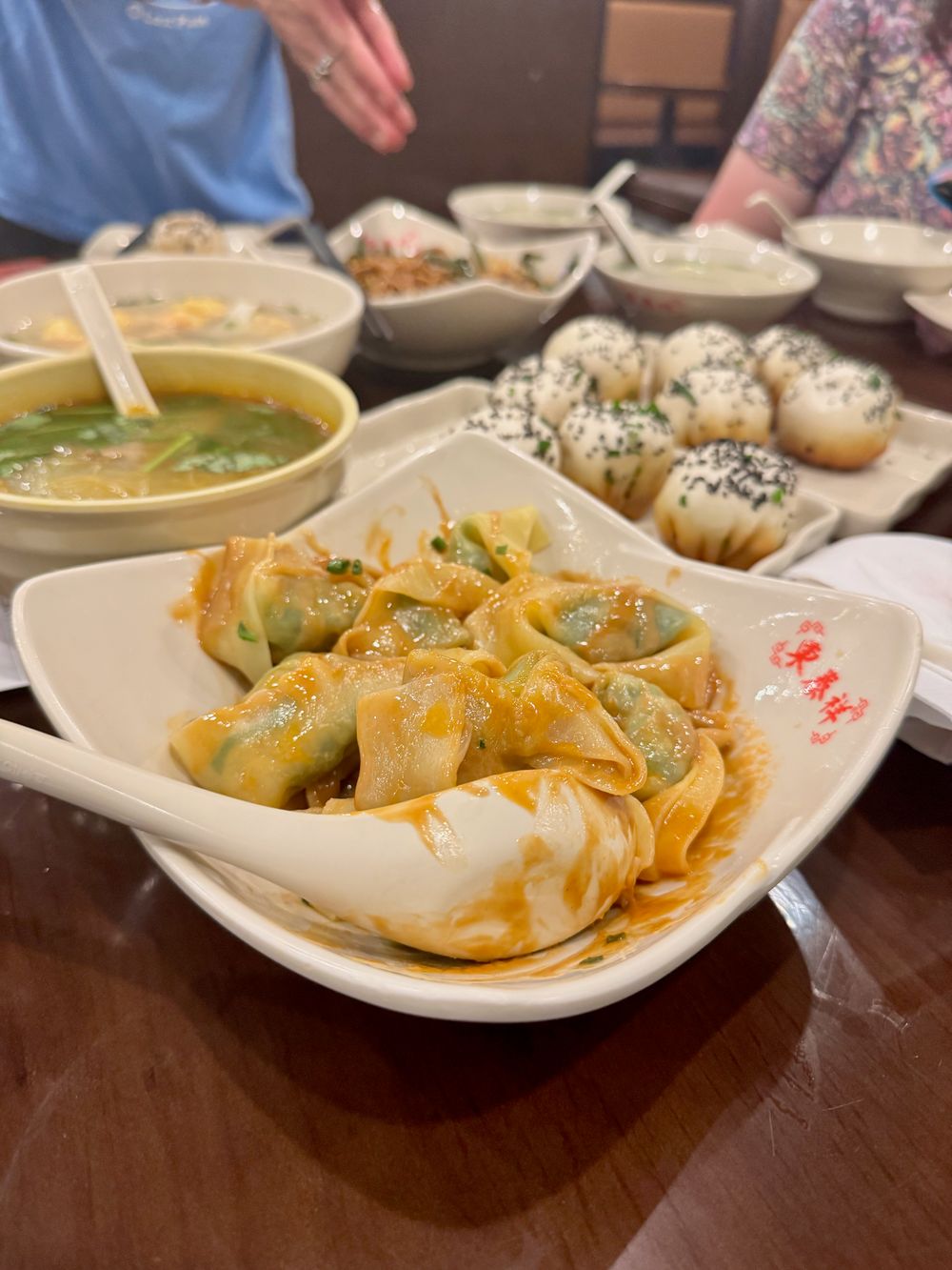 White bowl of wontons in orange chili oil and pan-fried sesame buns on a wooden table, Dapuqiao Shanghai fall 2025